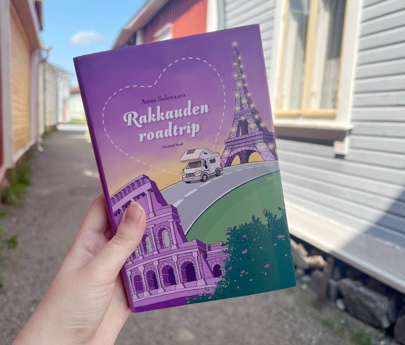 Rakkauden roadtrip -kirjan kansi pirteän violetti ja siinä on matkailuauto Eiffel-tornin ja Colosseumin välissä